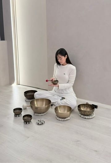 Bowa 穿著白色衣服坐在頌缽之間